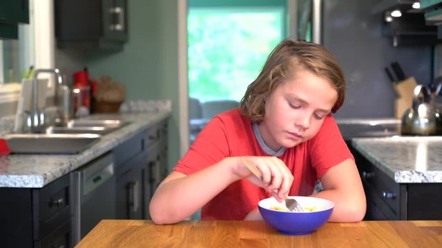 A ten-year-old boy eating a bowl of pasta in cheese sauce.  Mac and cheese.
