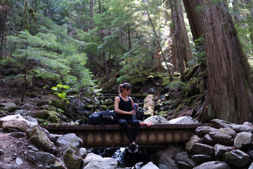 Young woman backpacker sitting on the wooden bridge in the forest