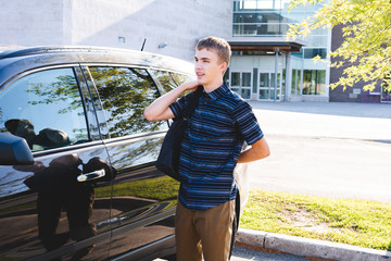 Teenager standing beside his car and putting on his backpack before school.