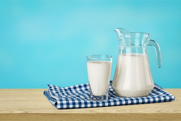 A glass of milk and a milk jug on plaid tablecloth