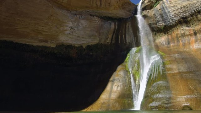 Lower Calf Creek waterfall flowing as it stands out from the shade on the cliffs.