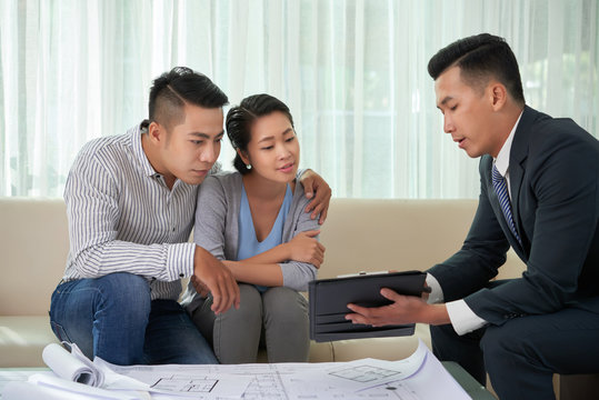 Real estate broker showing photos of house on digital tablet to young couple