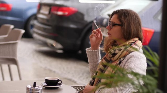 Woman sit smoking cigarette at the street cafe table while drinking coffee