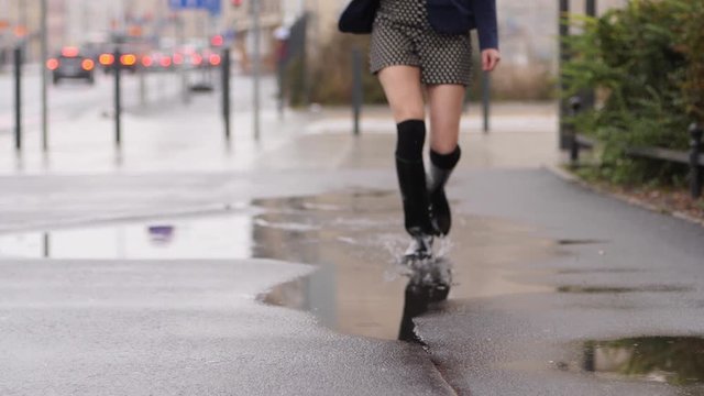 Good mood for rainy weather woman in rubber boots with high bootleg run in puddle with splash
