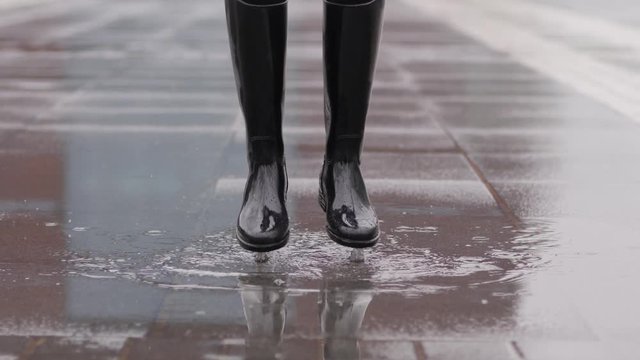 Good mood for rainy weather woman in rubber boots with high bootleg jump in puddle with splash