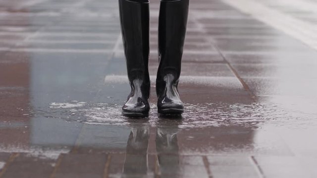 Good mood for rainy weather woman in rubber boots with high bootleg jump in puddle with splash