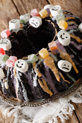 Delicious festive black Bundt cake with candied fruits, marshmelow and colored glaze close-up. vertical