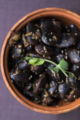 A small clay cup full with beans on a purple tablecloth