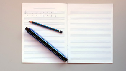 A harmonica and a pencil on an empty staff paper notebook