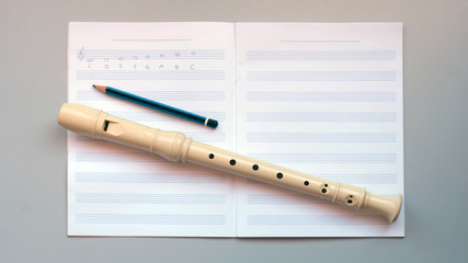 A recorder and a pencil on an empty staff paper notebook © CloudyTheater