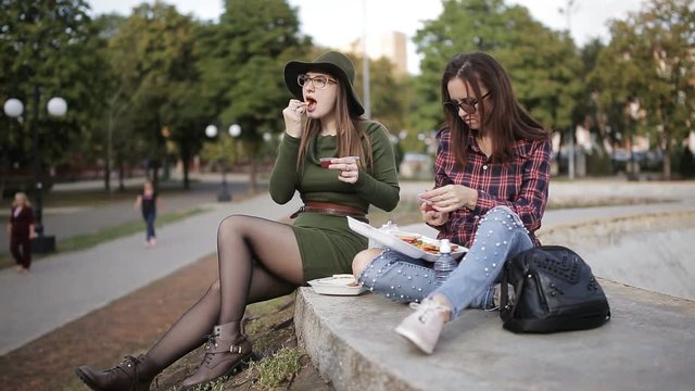 Urban picnic in the Park. Two girls hipster talk and eat sandwiches. The holiday sandwich.