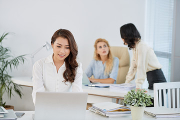 Pretty young Asian business lady working on laptop at her table in office