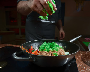 Caucasian chief cook cooking on the wok pan with flambe on the asian restaurant kitchen