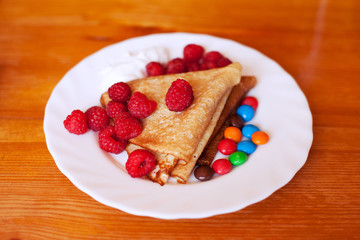 delicious pancakes with raspberries, sweets and sour cream lie on a white plate, breakfast in the hotel
