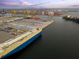 Aerial view of logistics concept commercial vehicles, cars and pickup trucks waiting to be load on to a roll-on/roll-off car carrier ship at Laem Chabang dockyard in Chonburi Province, Thailand