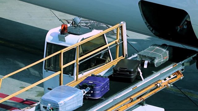 Unloading the luggage from the fuselage of aircraft. The baggage ride on the conveyor when unloading the air plane.