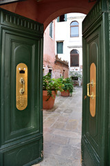 Open, wooden, green door leading to the courtyard of a tenement house in Italy.