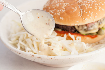 Salad with sauce and cheeseburger on a plate on the table