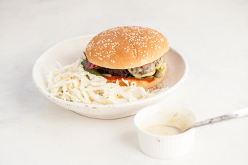 Salad with sauce and cheeseburger on a plate on the table