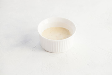 Bechamel sauce in a white bowl on a stone white table