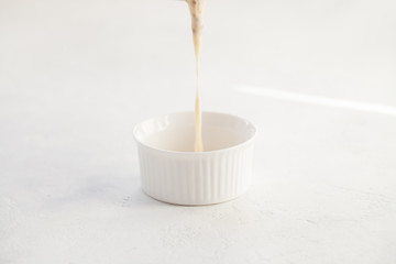 Pouring bechamel sauce into a white bowl on the table
