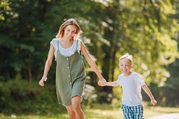 Sister teenager and little brother boy run their hands through park, sun light. Concept family sport.