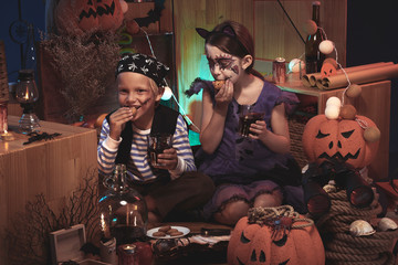 Children in costumes of pirate and cat having punch and cookies at Halloween party