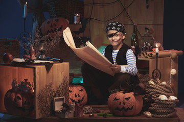 Smiling little pirate in Halloween costume holding big map and looking at camera