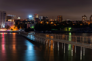 Fototapeta na wymiar Old long metal pier over the river. Night city landscape