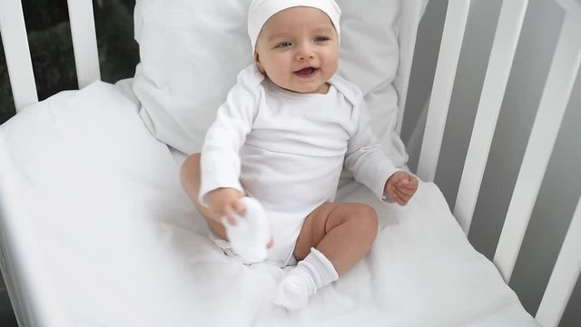 adorable baby in white clothes sitting in crib and smiling at home
