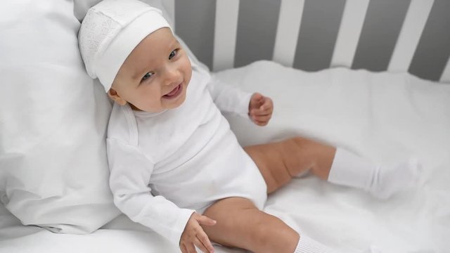 happy adorable baby in white clothes sitting in crib at home
