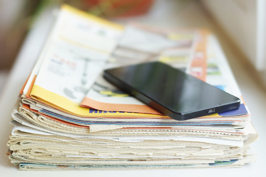 Stack of newspapers and magazines and smartphone. Pile of papers with news and mobile phone. Different sources of information - paper pages or screen of electronic device   