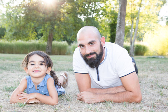 bald beard man lying on park grass with cute brunette daughter outdoor