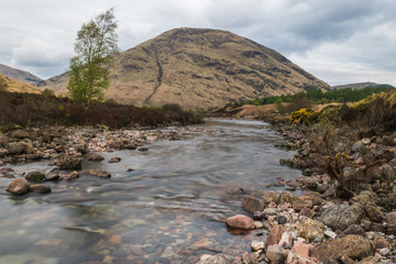 Glencoe river with smooth water flow and cloudy day. hill views at the back