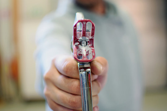 Man Pointing A Used Airless Paint Spray Gun At Camera. Shallow Depth Of Field.