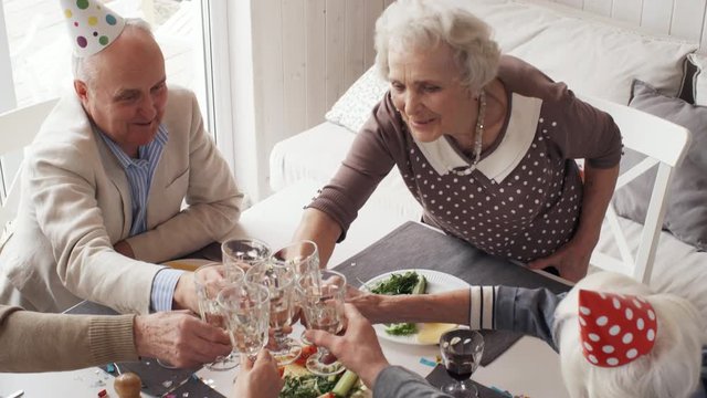 High angle shot of happy senior woman toasting with guests while drinking wine at birthday dinner party