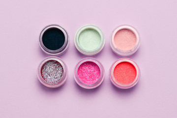 Cosmetics. Makeup. Jars with  crumbly bright shadows, glitter. Pink, green, lilac colors on lilac background. Closeup. Space for text or design.