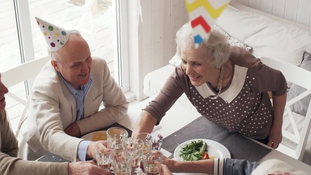 High angle view of elderly friends in party hats having holiday dinner and toasting with champagne