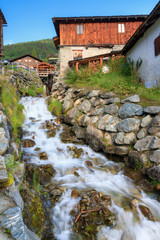 Fototapeta na wymiar Beautiful small creek running past the ancient sawmill with water wheel in the picturesque village of Grimentz, Switzerland, in summer 