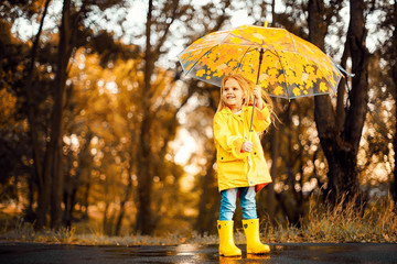 happy child girl with an umbrella and rubber boots in puddle on an autumn walk