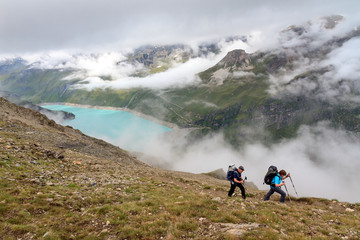 A couple with backpacks hiking on a summer day in the Swiss alps near Grimentz, Switzerland, with turquoise lake lac de Moiry in the background, on July 27, 2014
