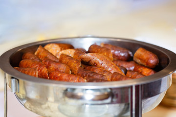 Cooked sausages sliced in half, placed in a large silver pot, served hot. Close up photo, selective focus