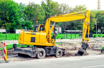 Large yellow excavator digs a hole, repairs the road, heavy equipment, road works.