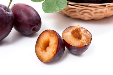 Yellow wooden basket with ripe plums, whole and half ripe plums isolated on a white background..