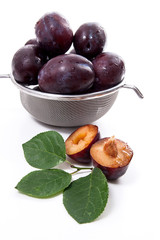 Steel colander with ripe plums, whole and half ripe plums with leaf isolated on a white background..