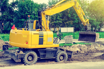 Large yellow excavator digs a hole, repairs the road, heavy equipment, road works.