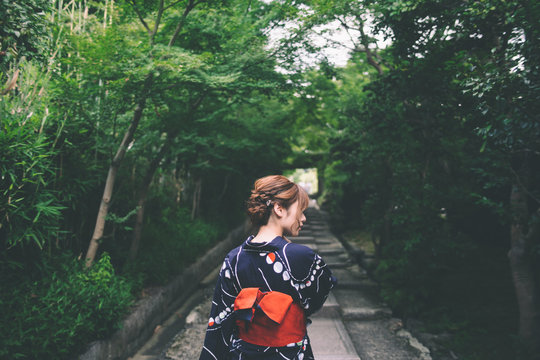 Rear view of young woman in traditional japanese clothing on treelined path