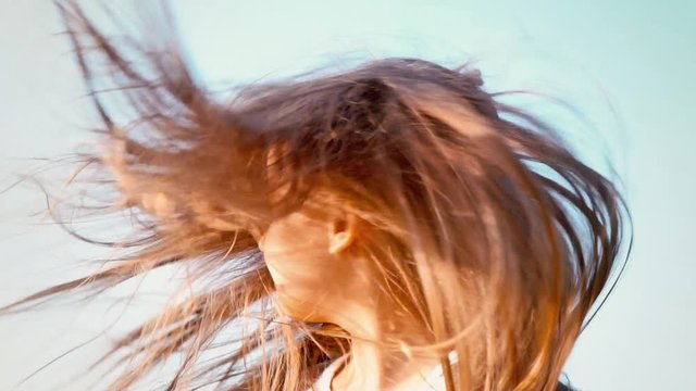 An attractive little girl with long flowing hair twists her head in different directions, girl playing with her hair in the wind, the wind develops long hair of the child