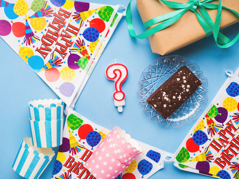 Happy Birthday party items flat lay. Gift box, decoration banner, paper glasses, chocolate cake. Question mark candle