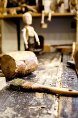 Brush and wooden hammer on a wooden table among the sawdust on the background of a finished wooden doll.
